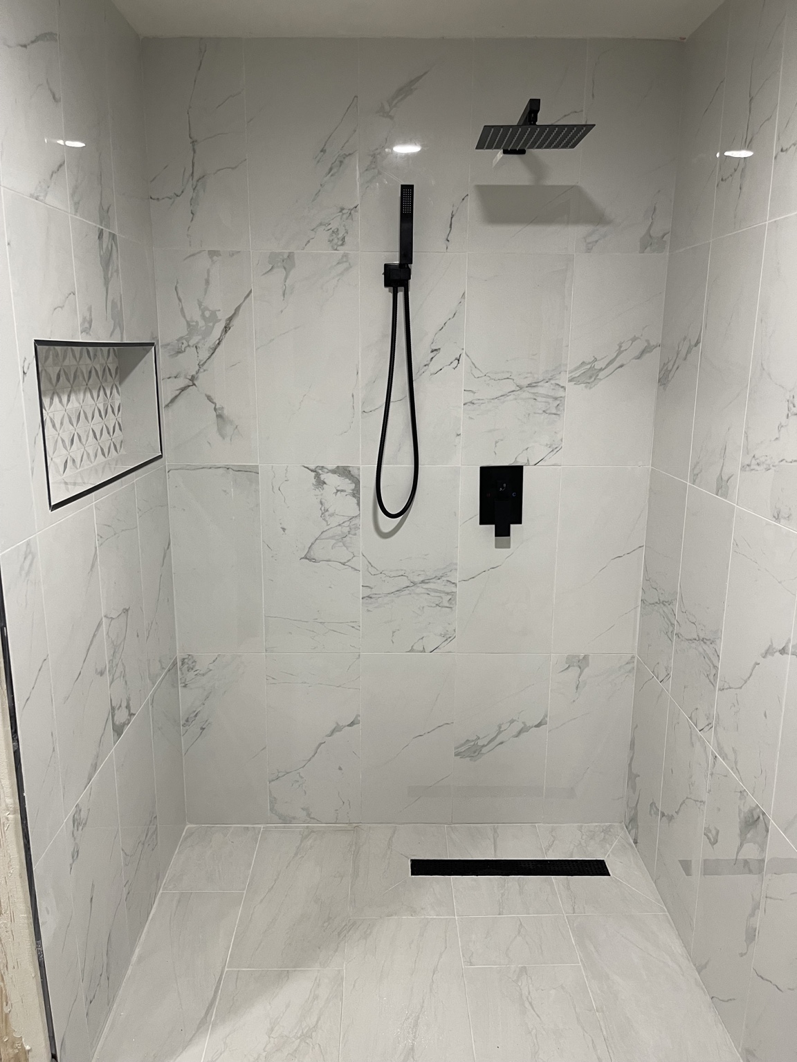 Finished tiled shower with black fixtures and linear drain